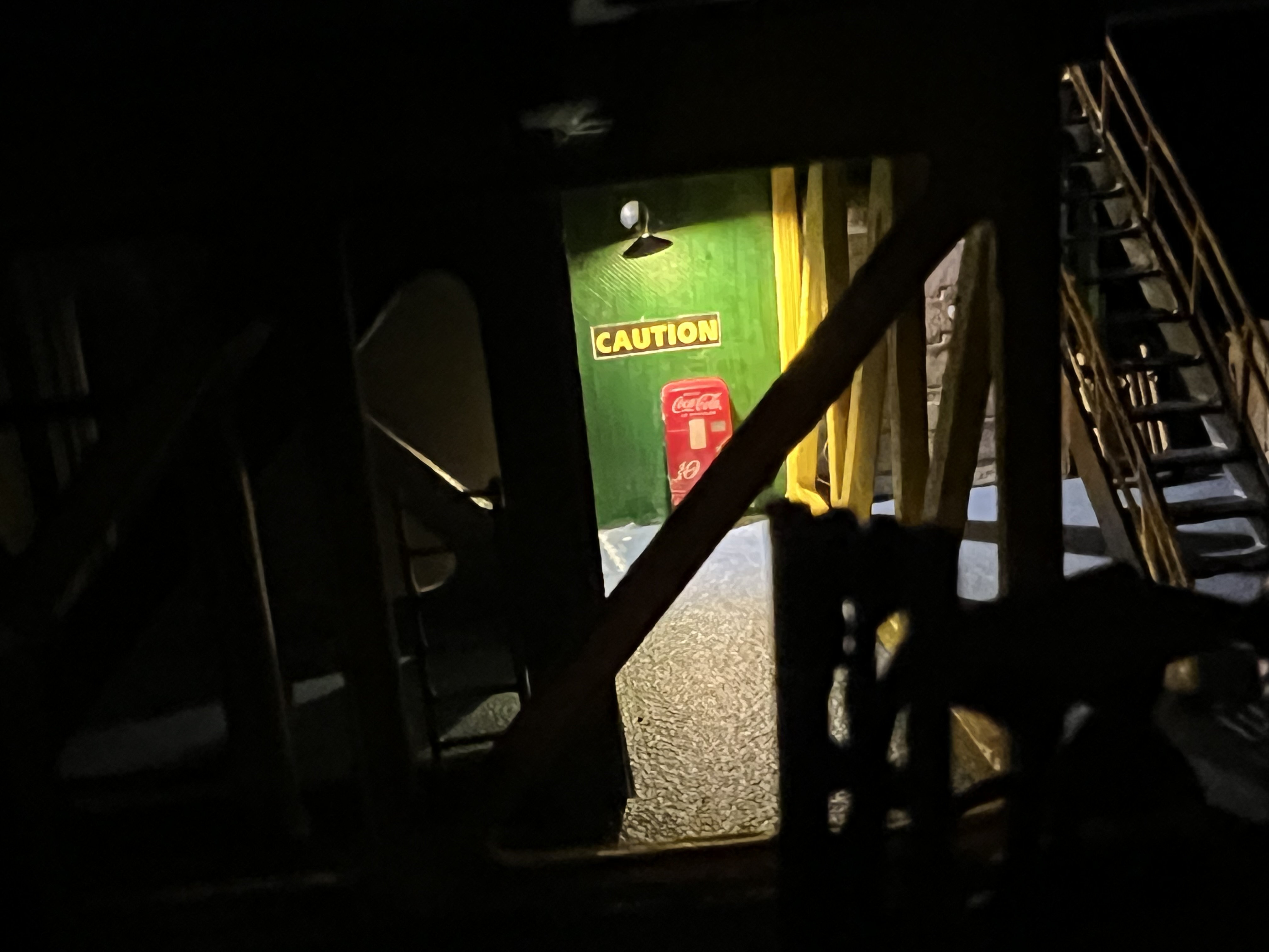 A tiny H0-scale Coca-Cola vending machine tucked into a back corner of the rig, spotlit by a gooseneck lamp.