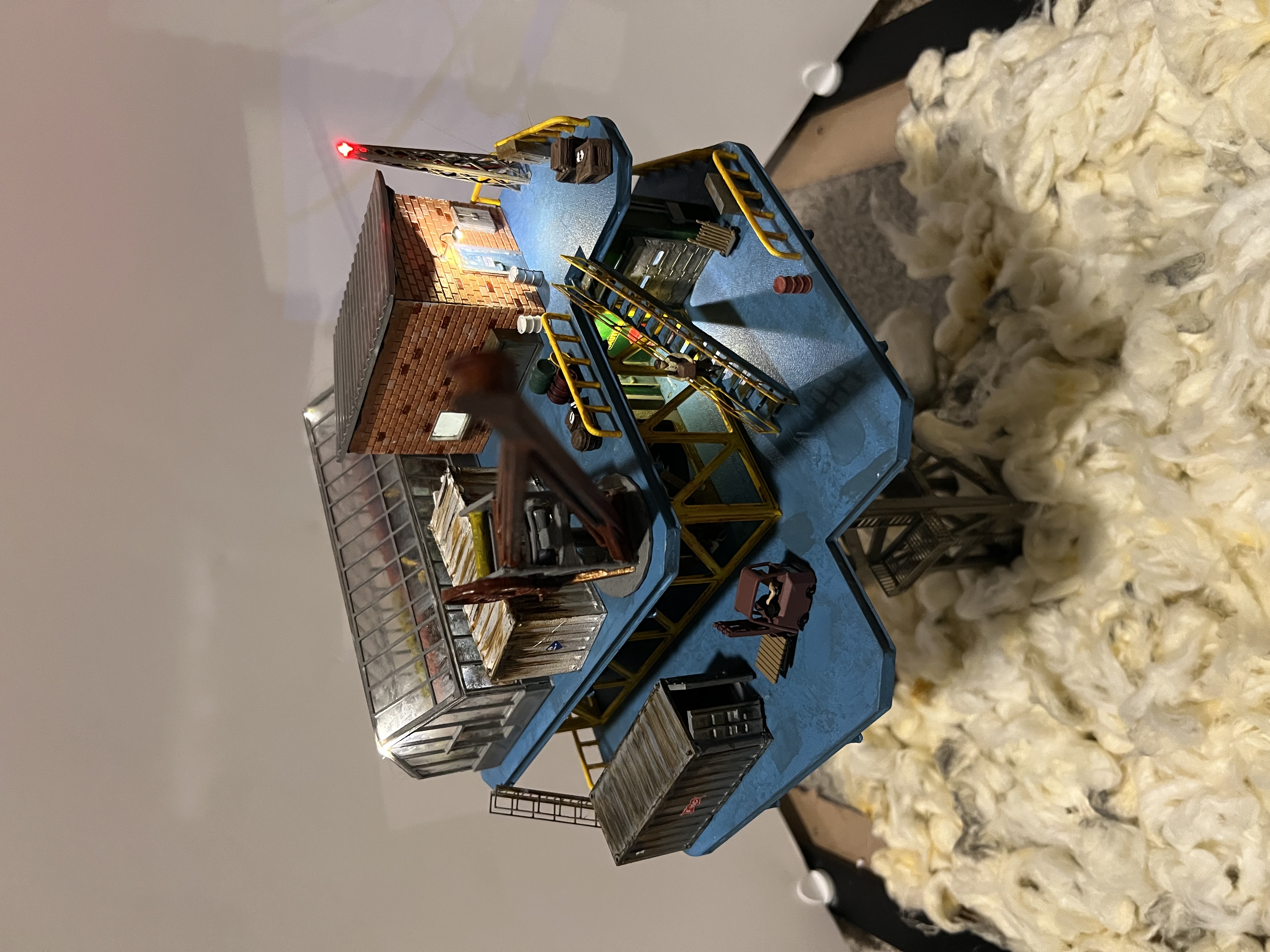 The finished drinkrig model: a tall lattice tower carrying stacked platforms, sheds and a greenhouse, standing in daylight above a bed of clouds.
