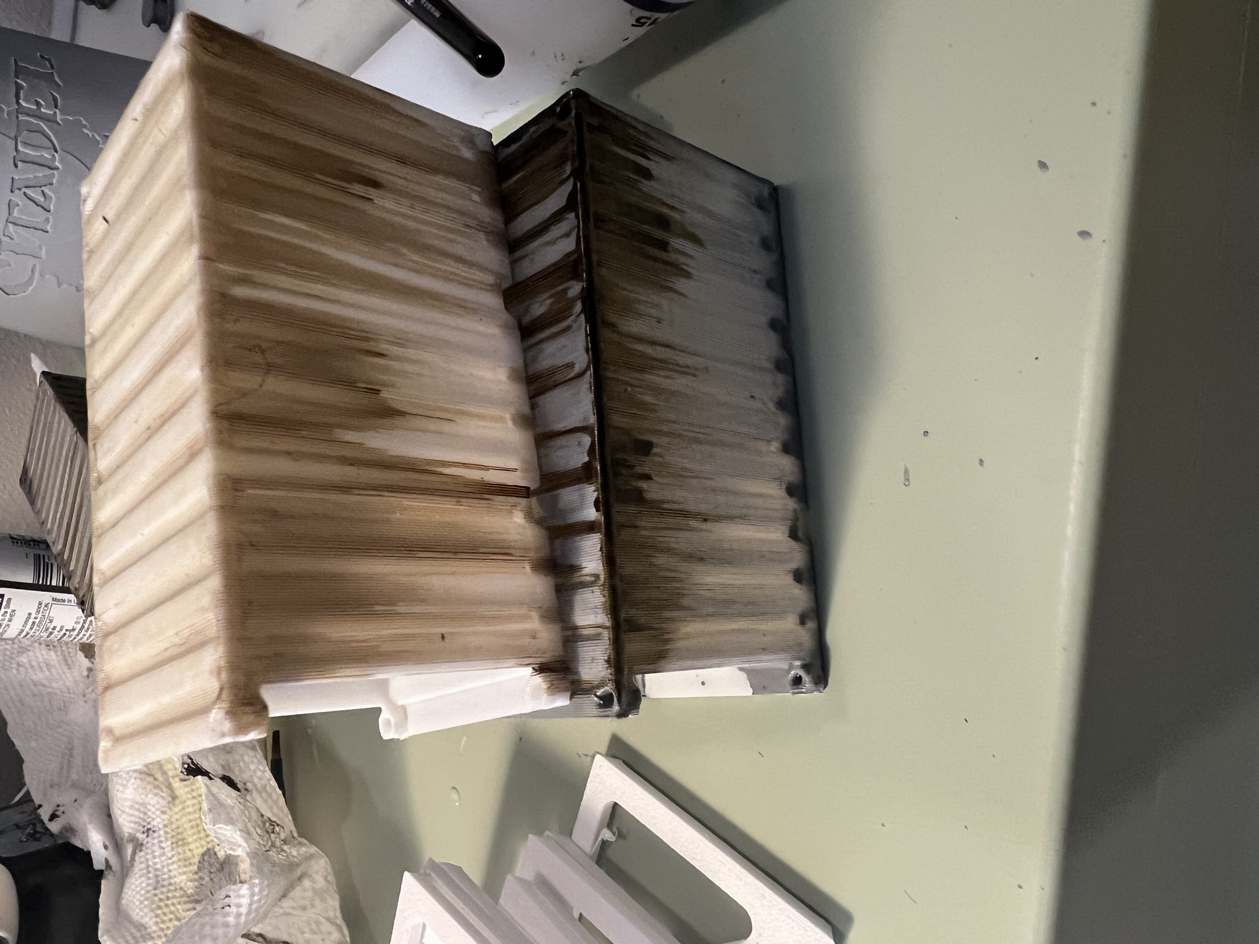 Two printed crates side by side; the upper one bare white plastic with a wash, the lower one primed first and noticeably smoother.
